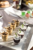 Una bandeja con diversos postres, como pasteles en capas y vasos pequeños con bebidas, probablemente para un bufé o evento.