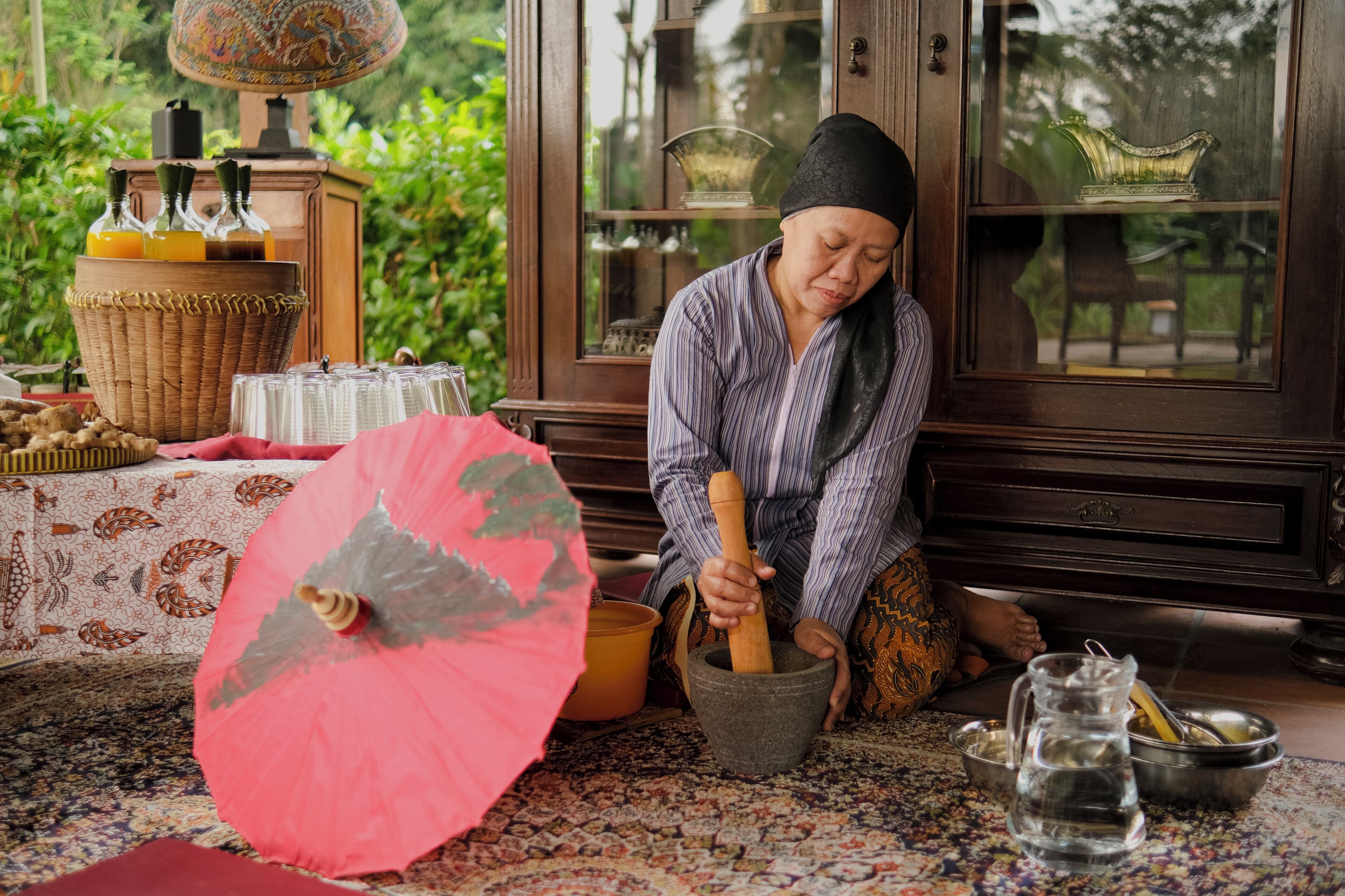 Uma pessoa usando um almofariz e pilão, uma cesta de vime, um guarda-chuva rosa e um armário de madeira com portas de vidro.