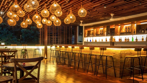 A bar area with wooden flooring, multiple bar stools, and hanging wicker light fixtures. - Plataran Heritage Borobudur Hotel (Borobudur)