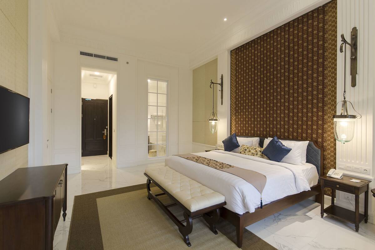 A bedroom with a large bed, bedside tables, a bench, and a TV.