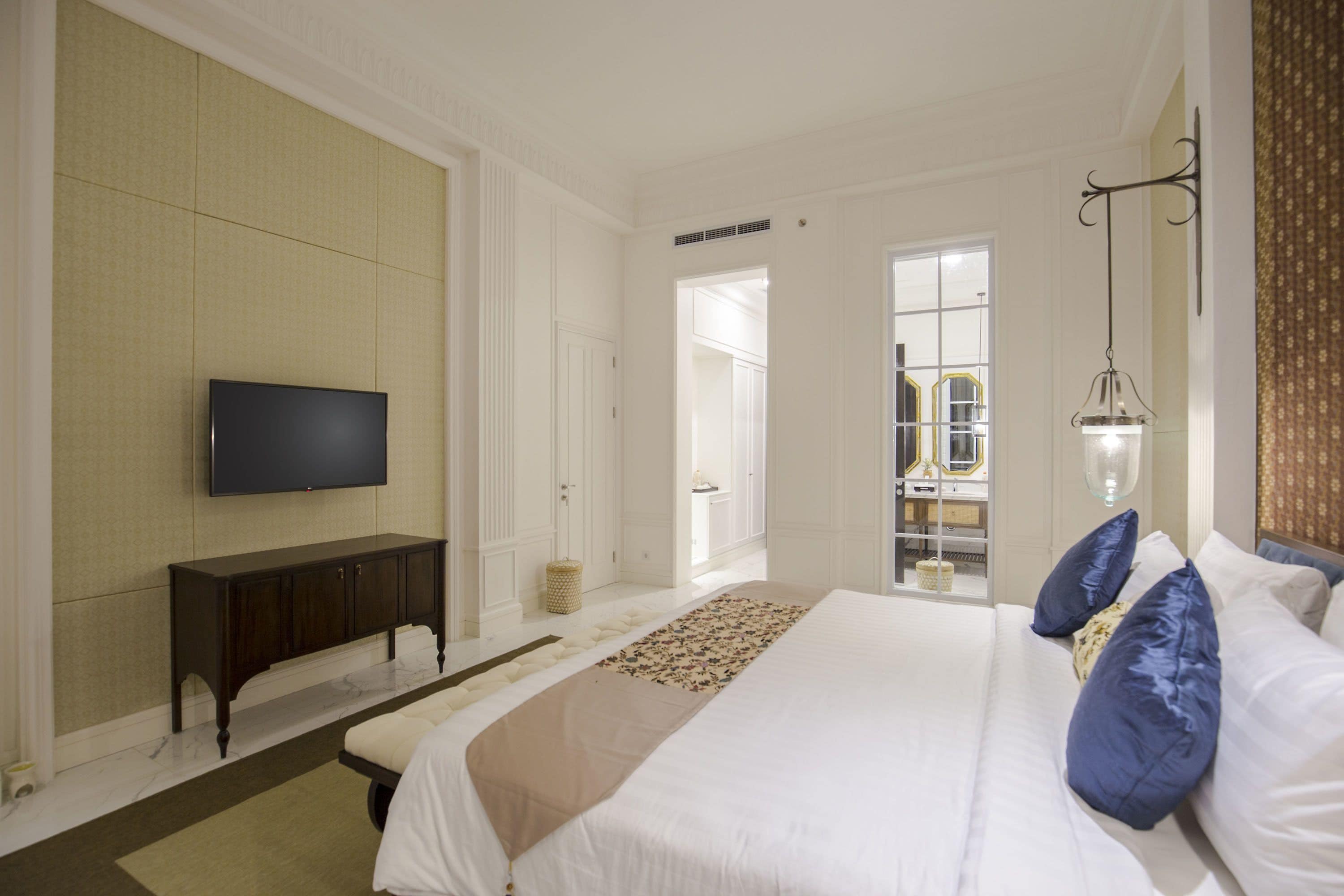 A hotel room with a large bed, a flat-screen TV, a bedside table, and a mirror.