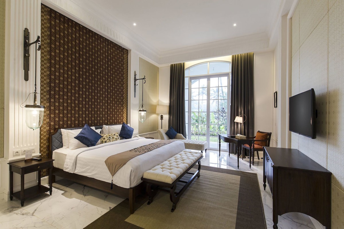 A spacious bedroom with a large bed, a desk, a chair, and a television.
