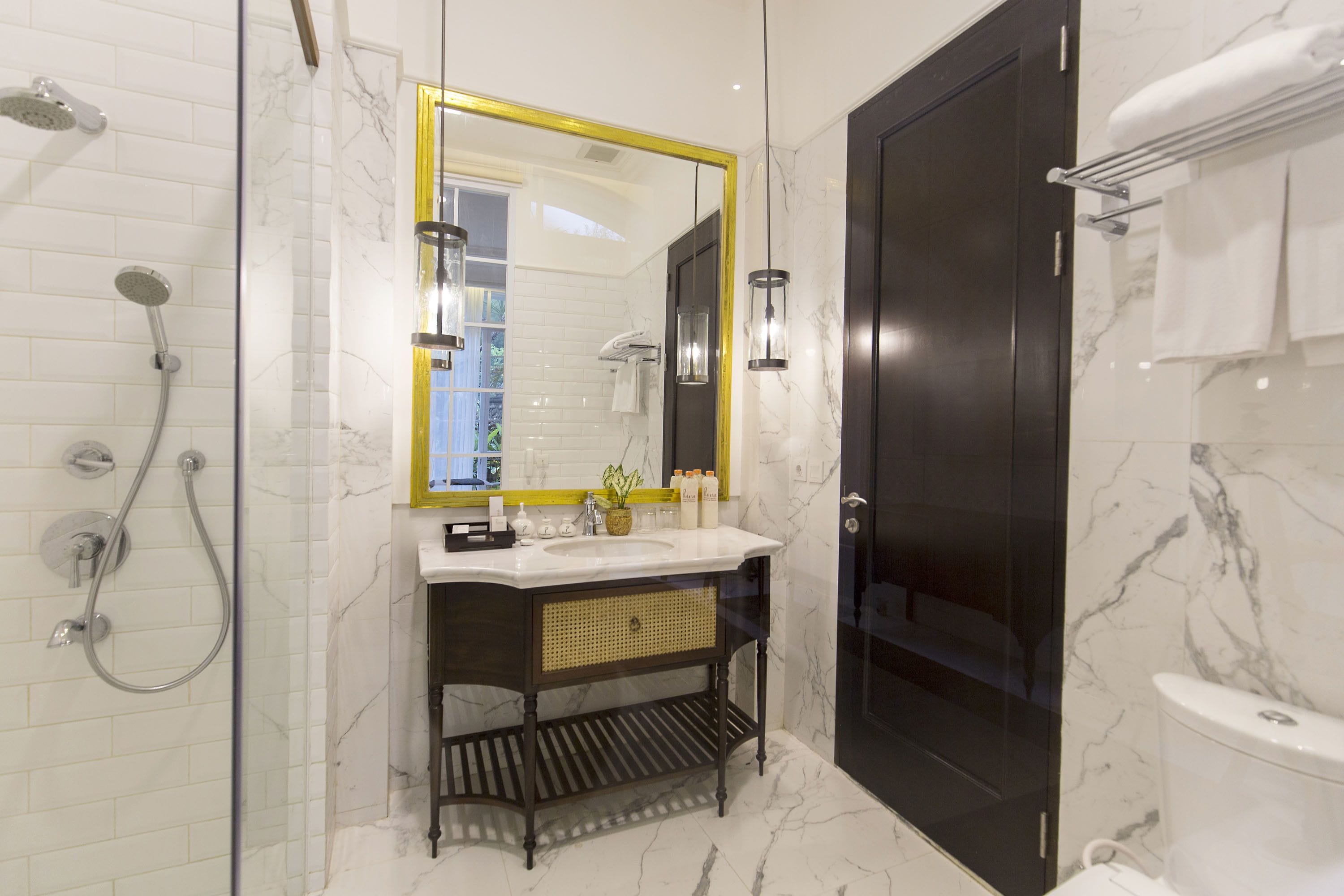 A modern bathroom with a glass-enclosed shower, a large mirror with a gold frame, a dark wooden vanity, and a marble floor.