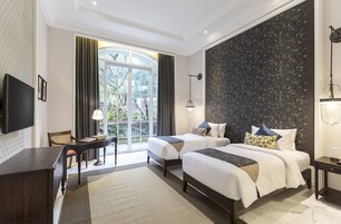 Habitación de hotel con dos camas, un escritorio, un televisor y un amplio ventanal con cortinas.