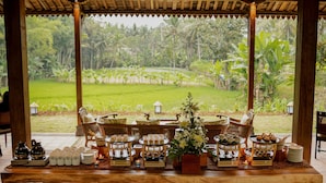 A wooden table set with various food items and a flower centerpiece, overlooking a lush garden with banana trees. - Plataran Heritage Borobudur Hotel (Borobudur)