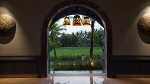 An arched doorway leading to a lush garden with palm trees and a reflective floor. - Plataran Heritage Borobudur Hotel (Borobudur)