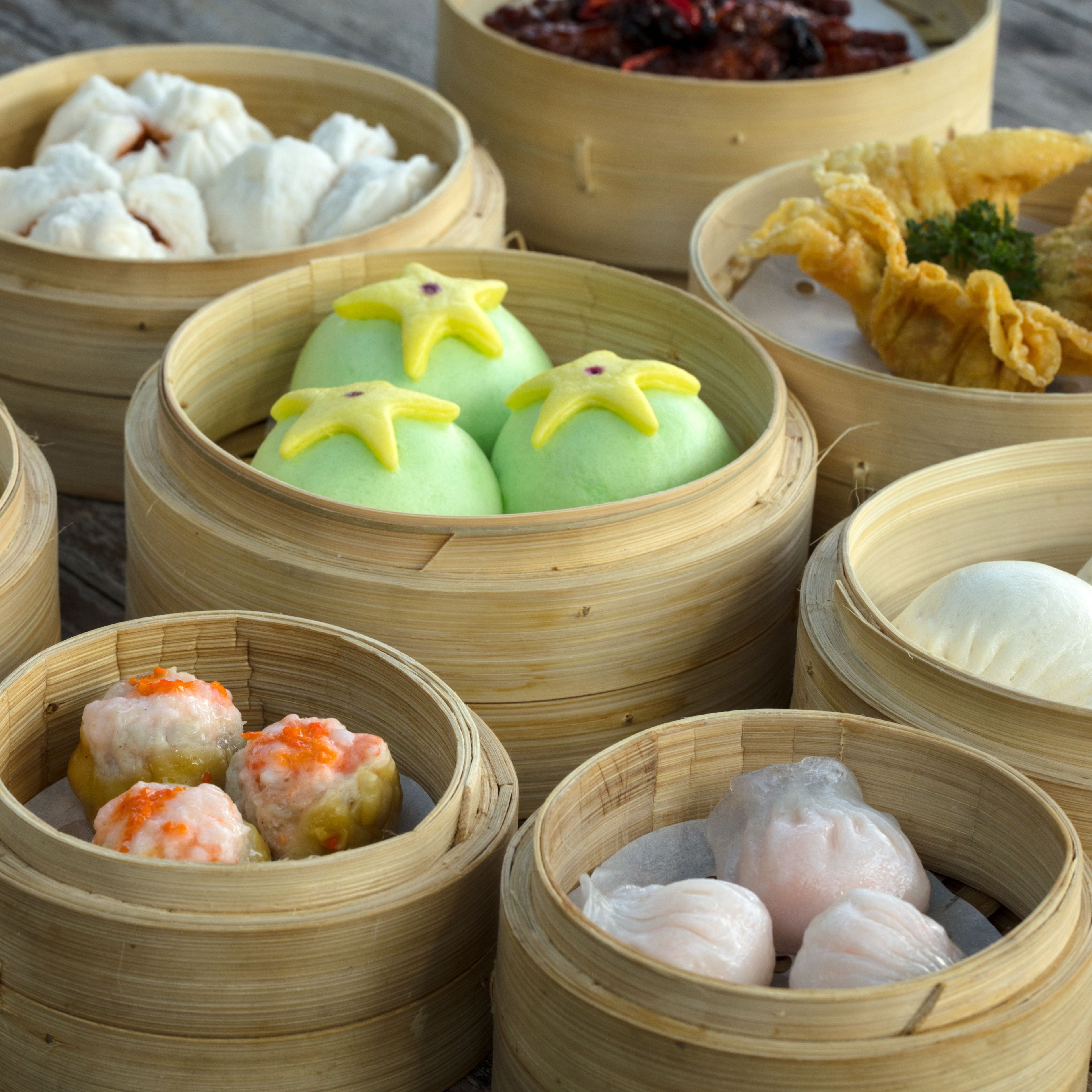 Variedad de platos de dim sum en vaporeras de bambú, incluyendo dumplings verdes con adornos amarillos, dumplings blancos y dumplings de camarón con huevas naranjas.
