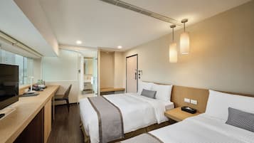 Habitació d'hotel amb dues llits, una taula de treball, una cadira, un televisor i un bany visible per una porta oberta.