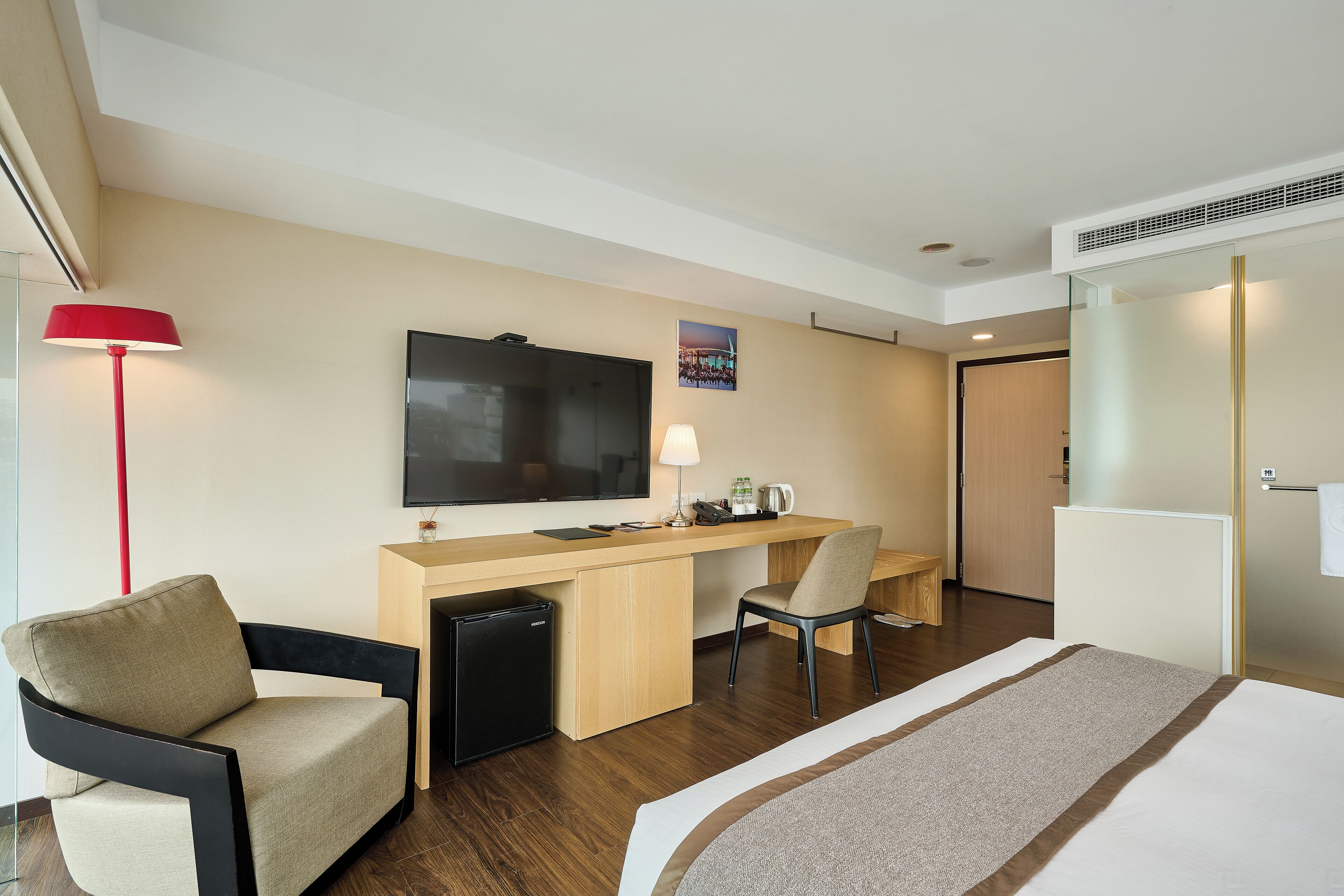 A hotel room with a bed, desk, chair, TV, and a small refrigerator.