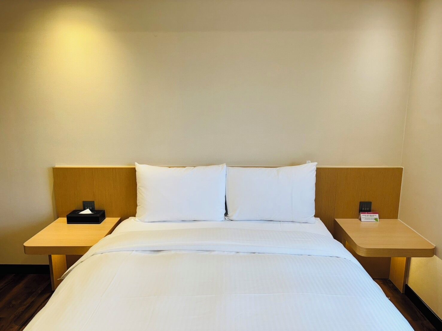 Quarto de hotel com uma cama grande, duas mesas de cabeceira e uma cabeceira de madeira.