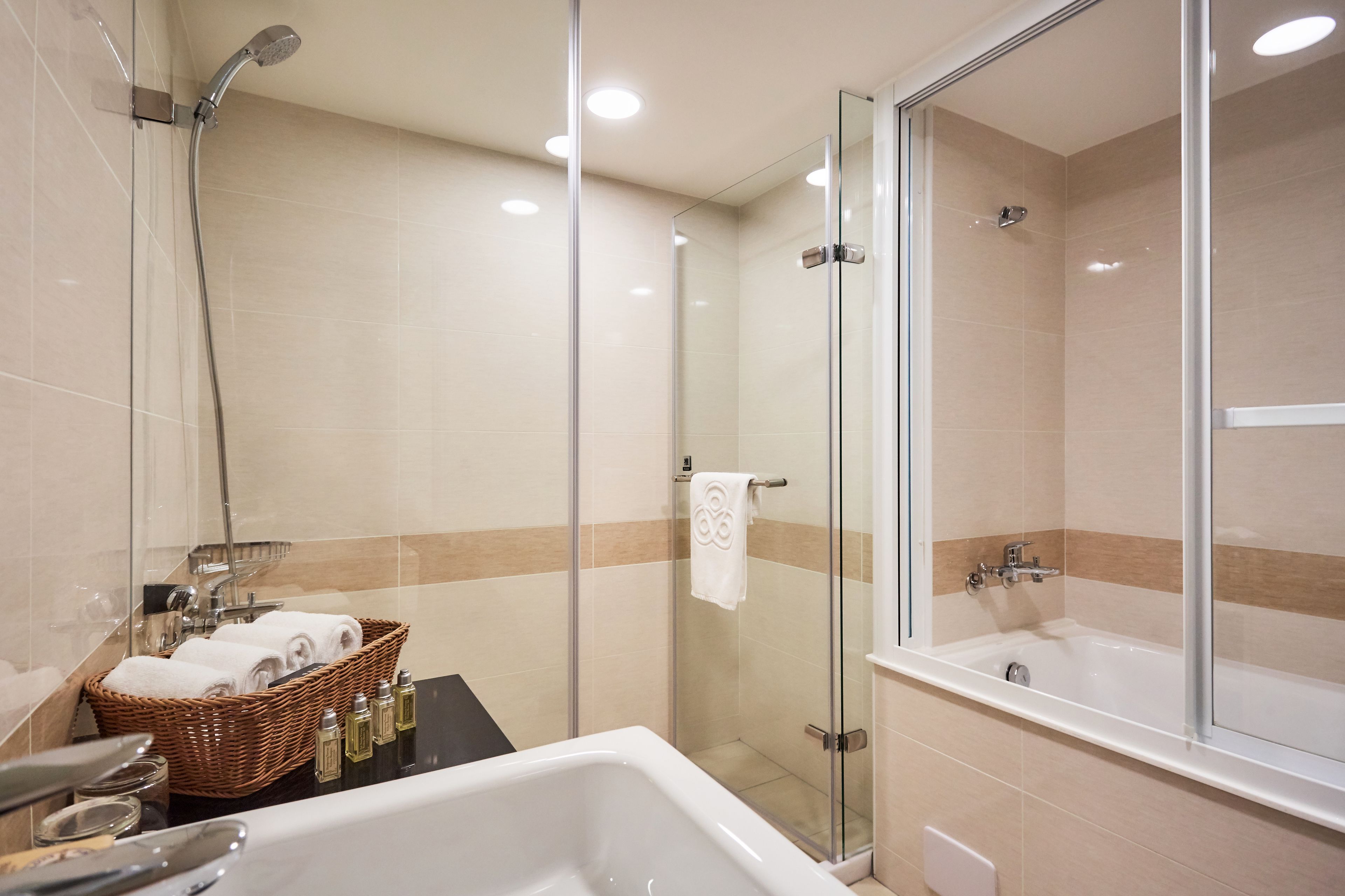 Een moderne badkamer met een douche met glazen wand, een vrijstaand bad en een rieten mand met handdoeken.