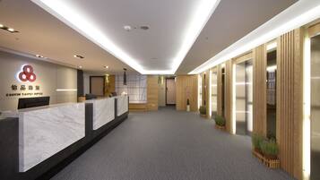 A hotel reception area with a marble counter, wooden paneling, and potted plants.