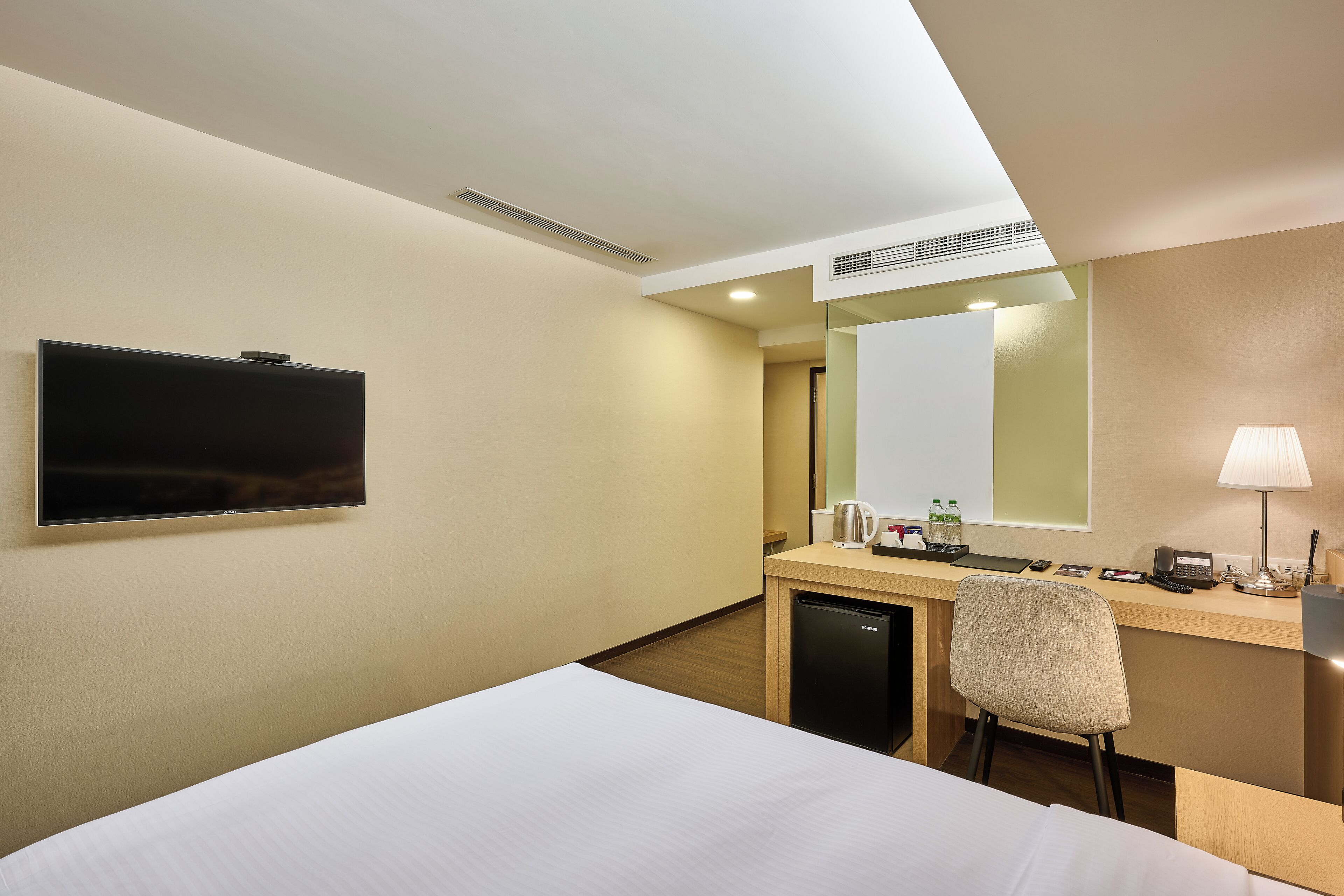 Ein Hotelzimmer mit Bett, Schreibtisch mit Stuhl, Fernseher, Spiegel und Lampe.