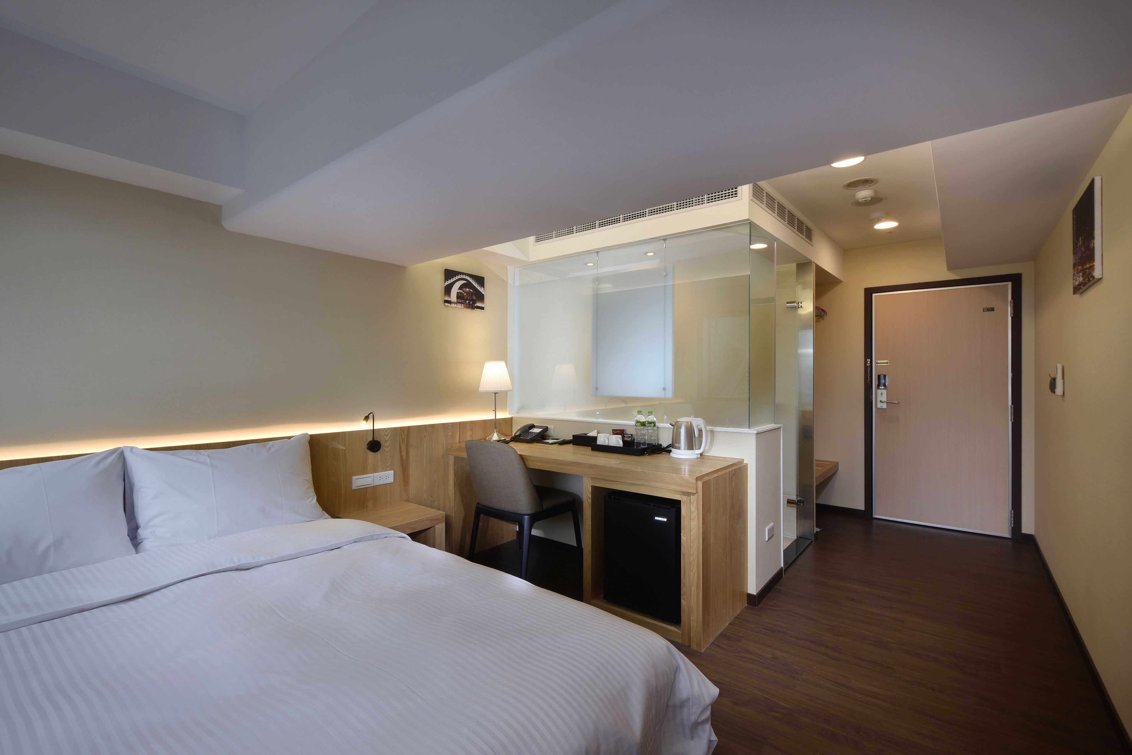 A hotel room with a bed, desk, chair, and a small kitchenette.