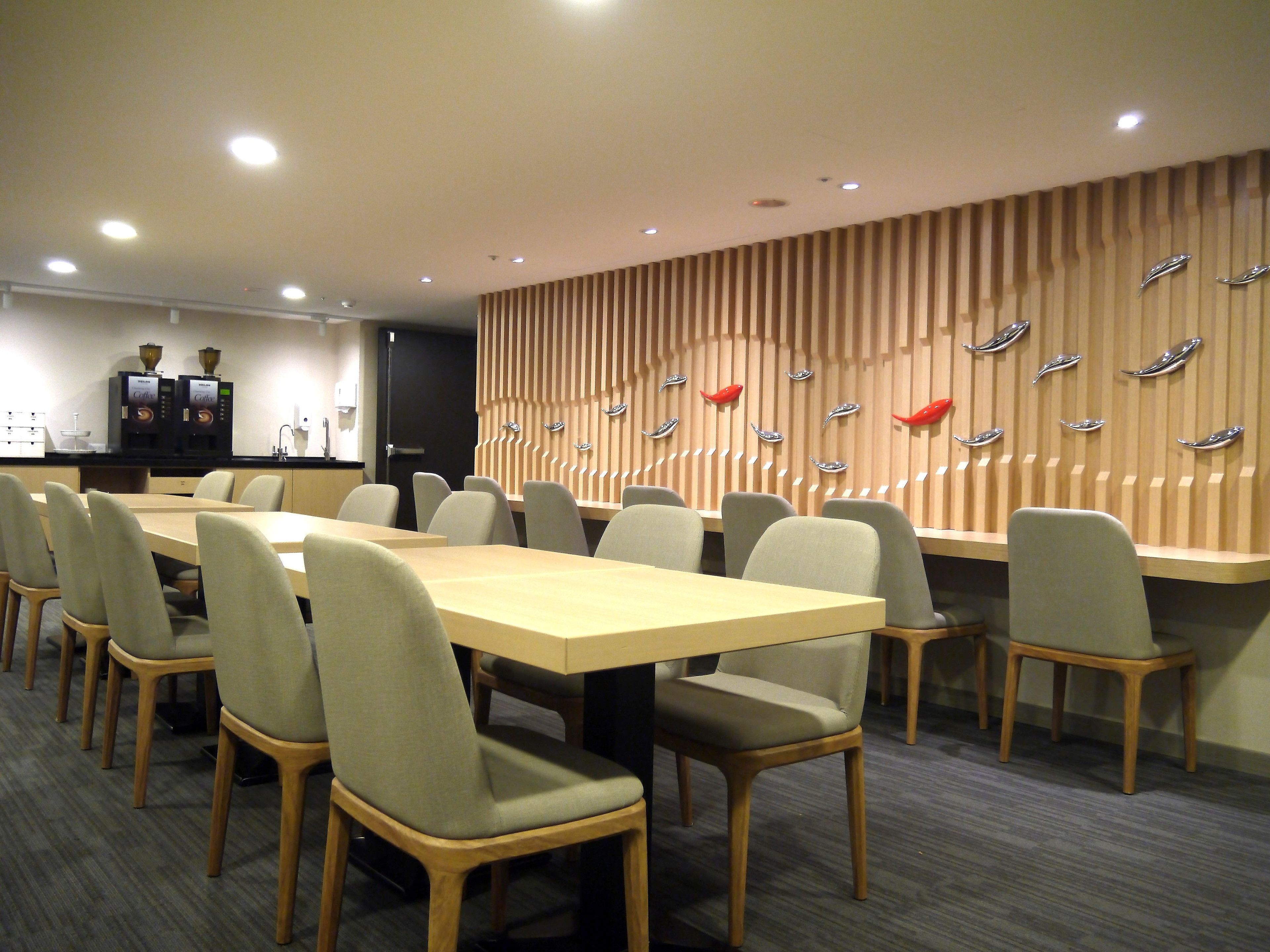 A conference room with a long table, multiple chairs, a coffee station, and a wall with decorative elements.