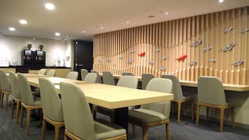 A conference room with a long table, multiple chairs, a coffee station, and a wall with decorative elements.