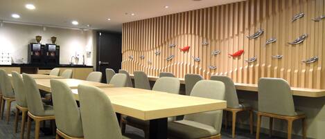 A conference room with a long table, multiple chairs, a coffee station, and a wall with decorative elements.