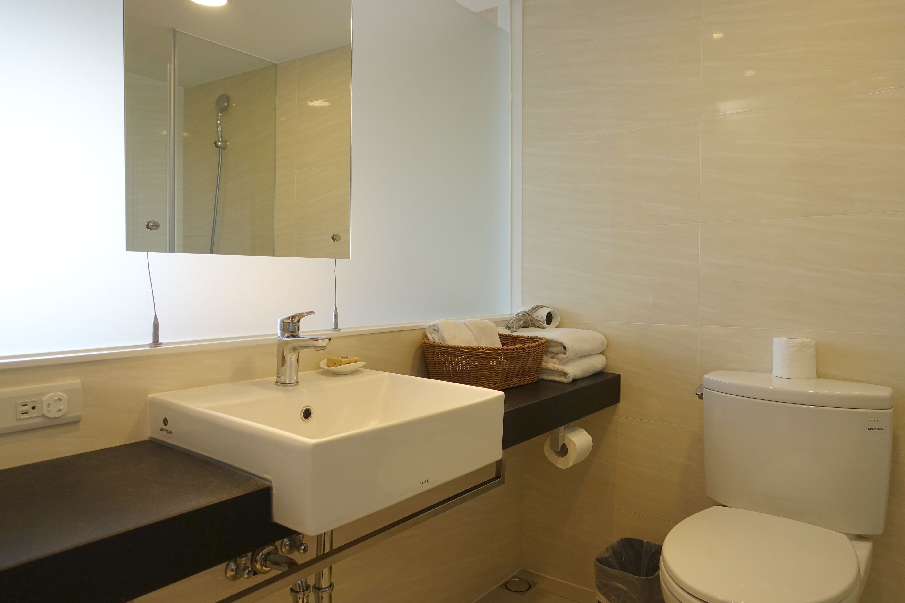 Een badkamer met een wit wastafel, een spiegel, een toilet en een prullenbak.