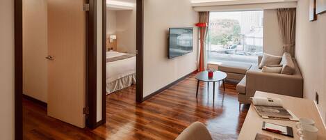 Une chambre d’hôtel avec un plancher en bois, un lit, une télévision, un canapé, une table à manger et une fenêtre donnant sur l’extérieur.