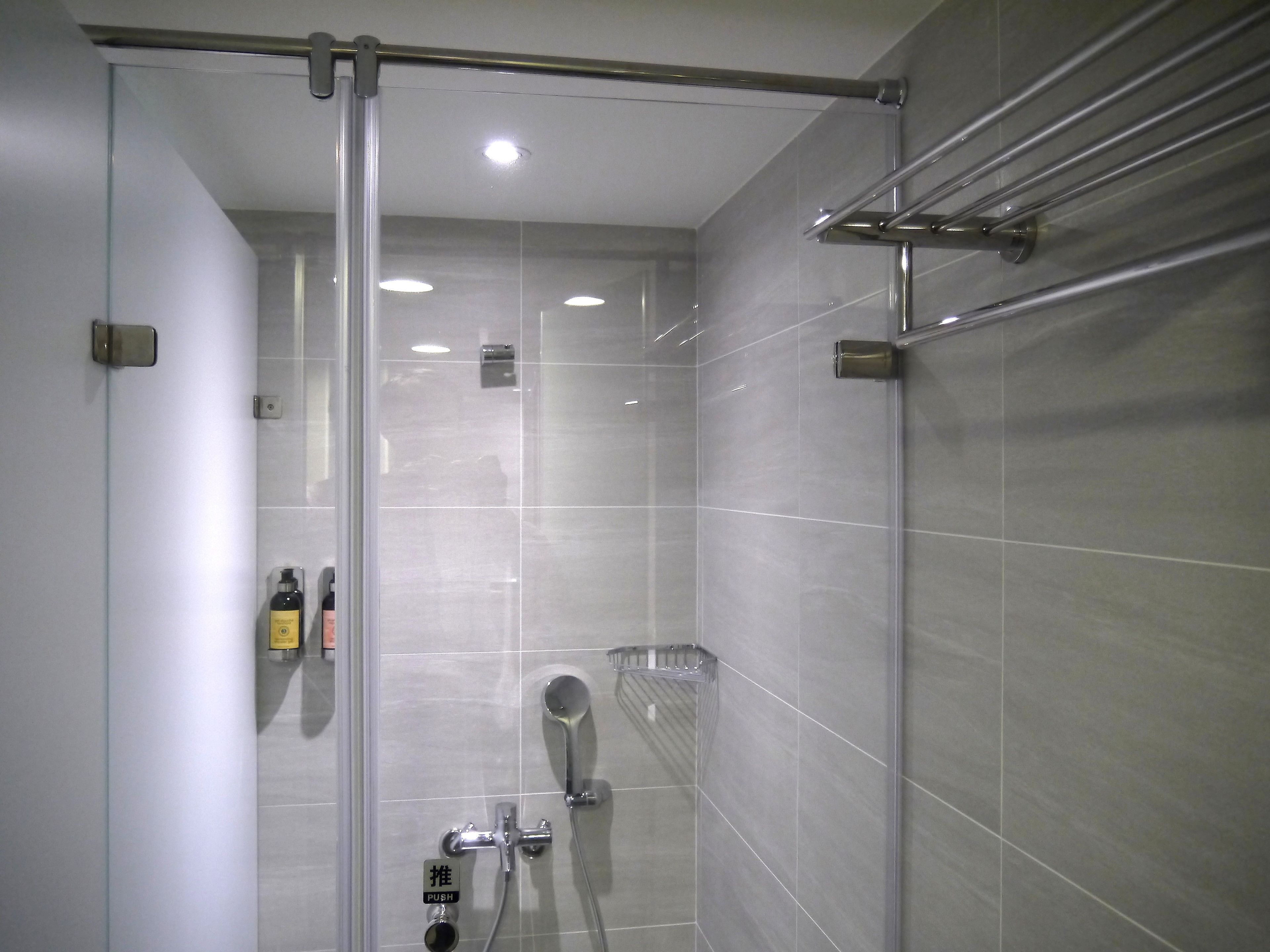 Une douche moderne dotée d’une porte en verre, d’un pommeau de douche à main et d’un porte-serviettes fixé au mur.