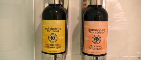 Two bottles of L'OCCITANE shower gel and shampoo on a marble surface.