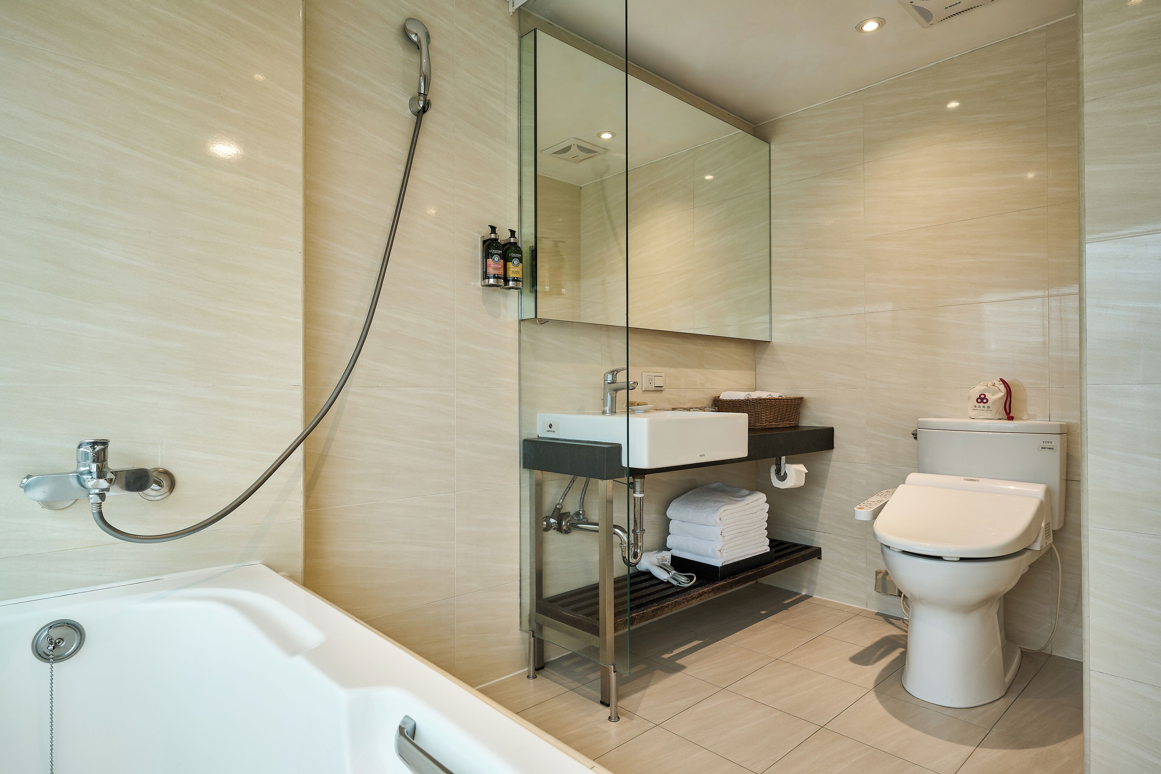 A modern bathroom with a bathtub, a toilet, and a glass-enclosed vanity.