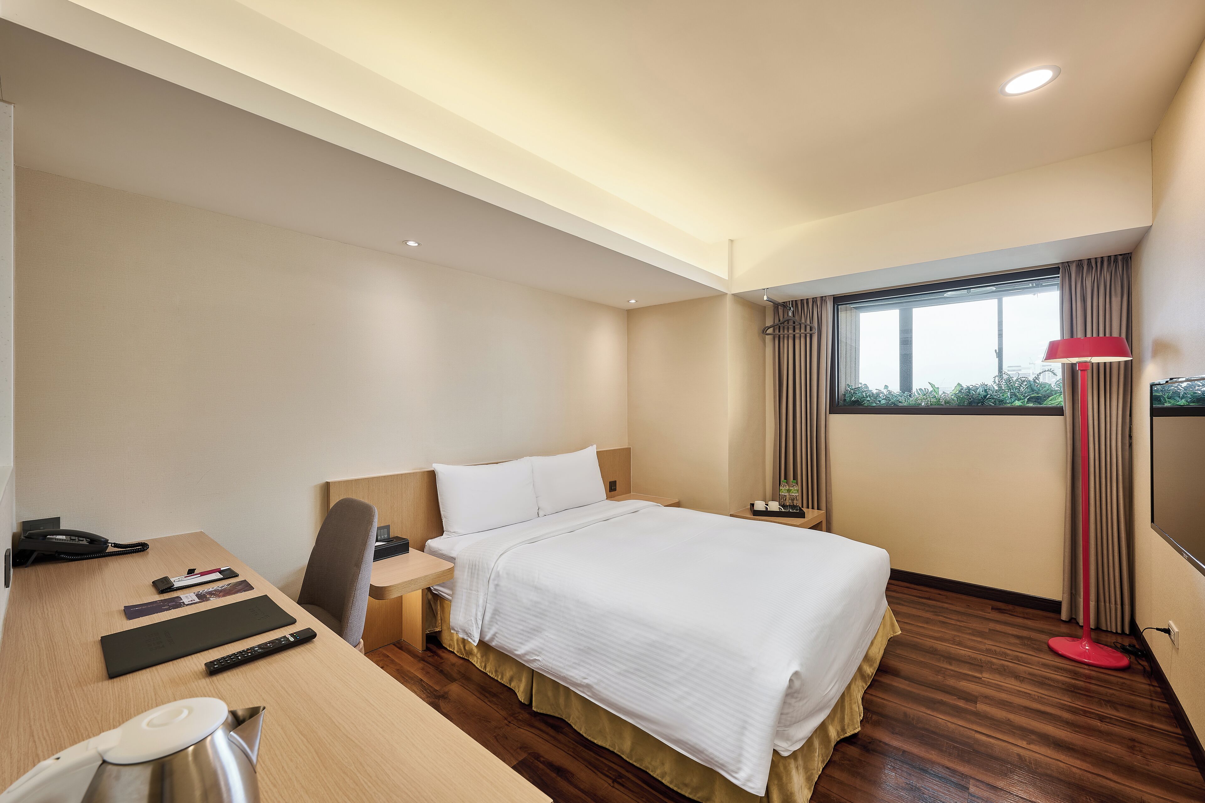 A hotel room with a bed, desk, chair, and a TV.