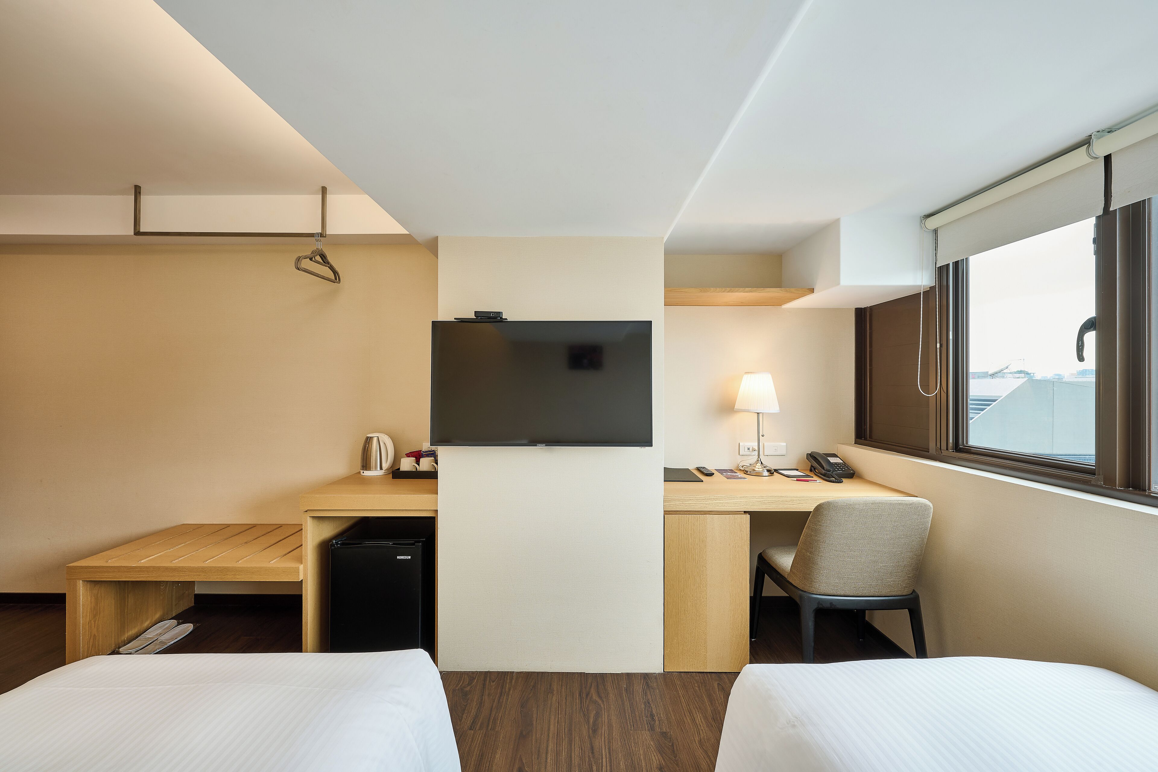 Hotelkamer met twee bedden, een bureau met een televisie, een stoel, een lamp en een raam met uitzicht.