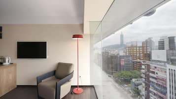 Una habitación de hotel moderna con un ventanal grande, un televisor de pantalla plana, una lámpara roja de pie y un sofá.