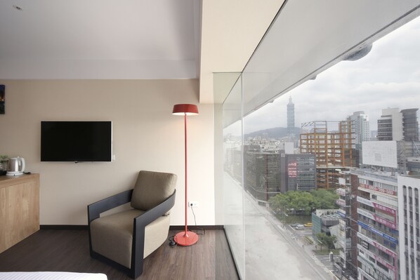 Una habitación de hotel moderna con un ventanal grande, un televisor de pantalla plana, una lámpara roja de pie y un sofá.