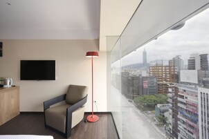 Moderni hotellihuone, jossa on suuri ikkuna, taulutelevisio, punainen lattiavalaisin ja sohva.