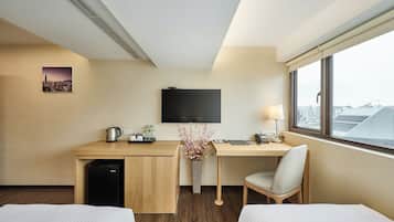 A hotel room with a bed, a desk with a computer, a TV, and a window with a city view.