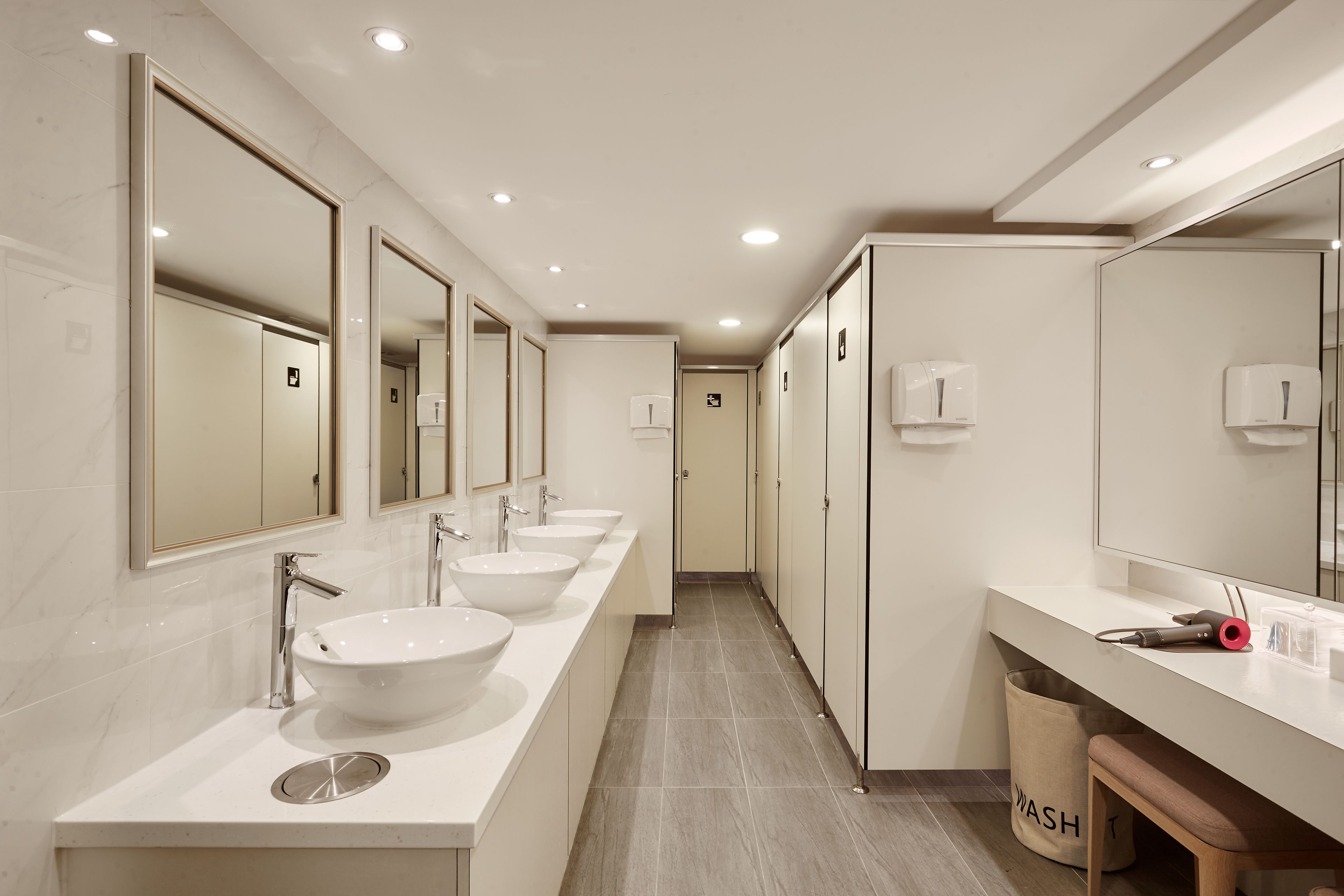 Een moderne badkamer met drie wasbakken, spiegels en een afvalbak.