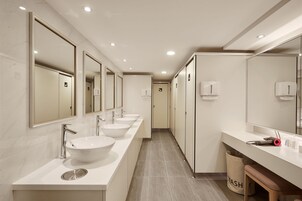 Een moderne badkamer met drie wasbakken, spiegels en een afvalbak.