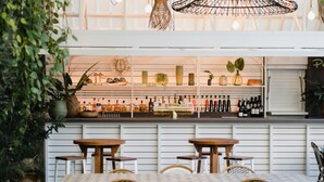 An indoor seating area with tables and chairs, a bar with shelves of bottles, and hanging light fixtures. - The Island Gold Coast (Surfers Paradise)