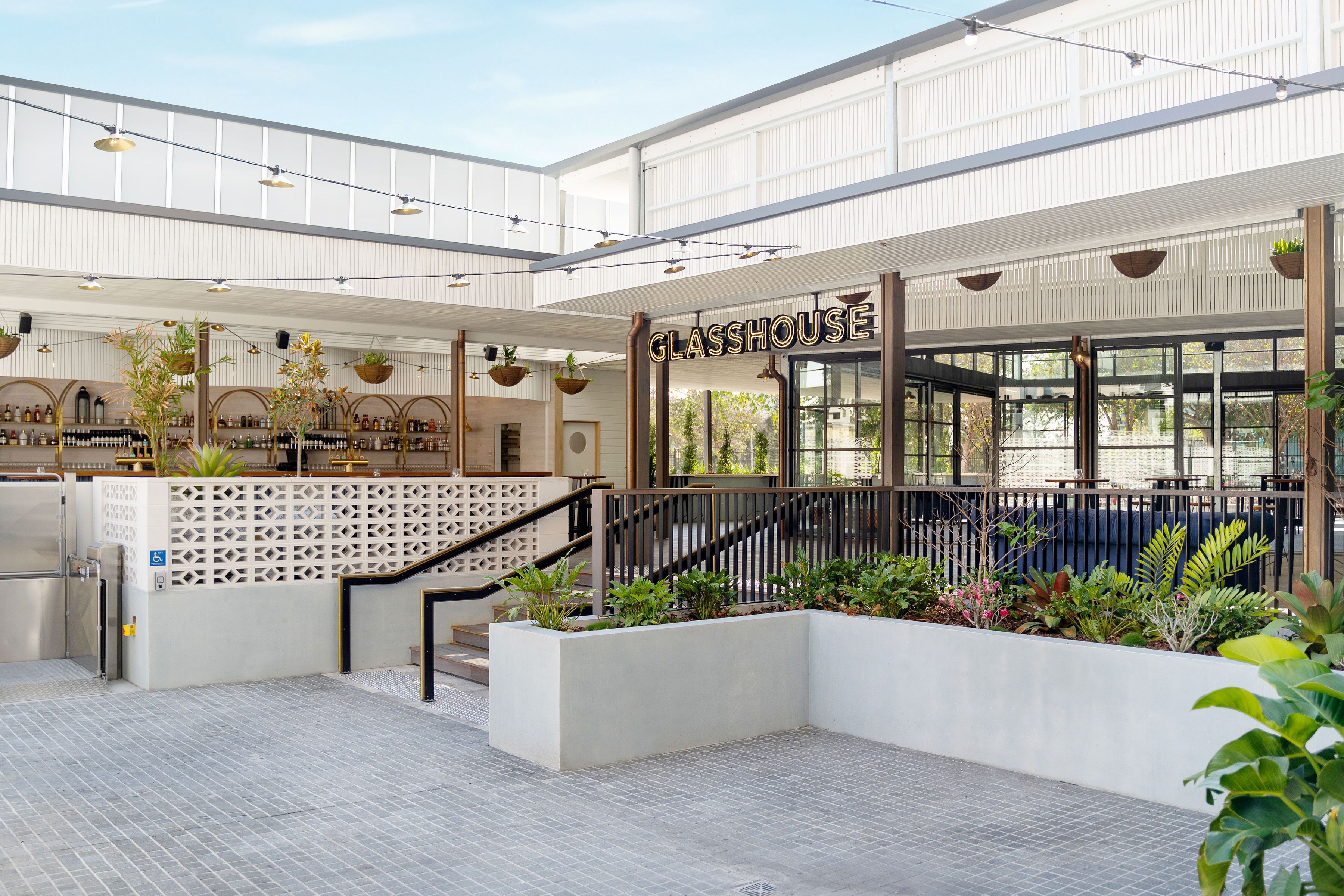 A spacious atrium with a modern design, featuring a staircase, hanging plants, and a visible bar area.