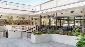 A spacious atrium with a modern design, featuring a staircase, hanging plants, and a visible bar area.