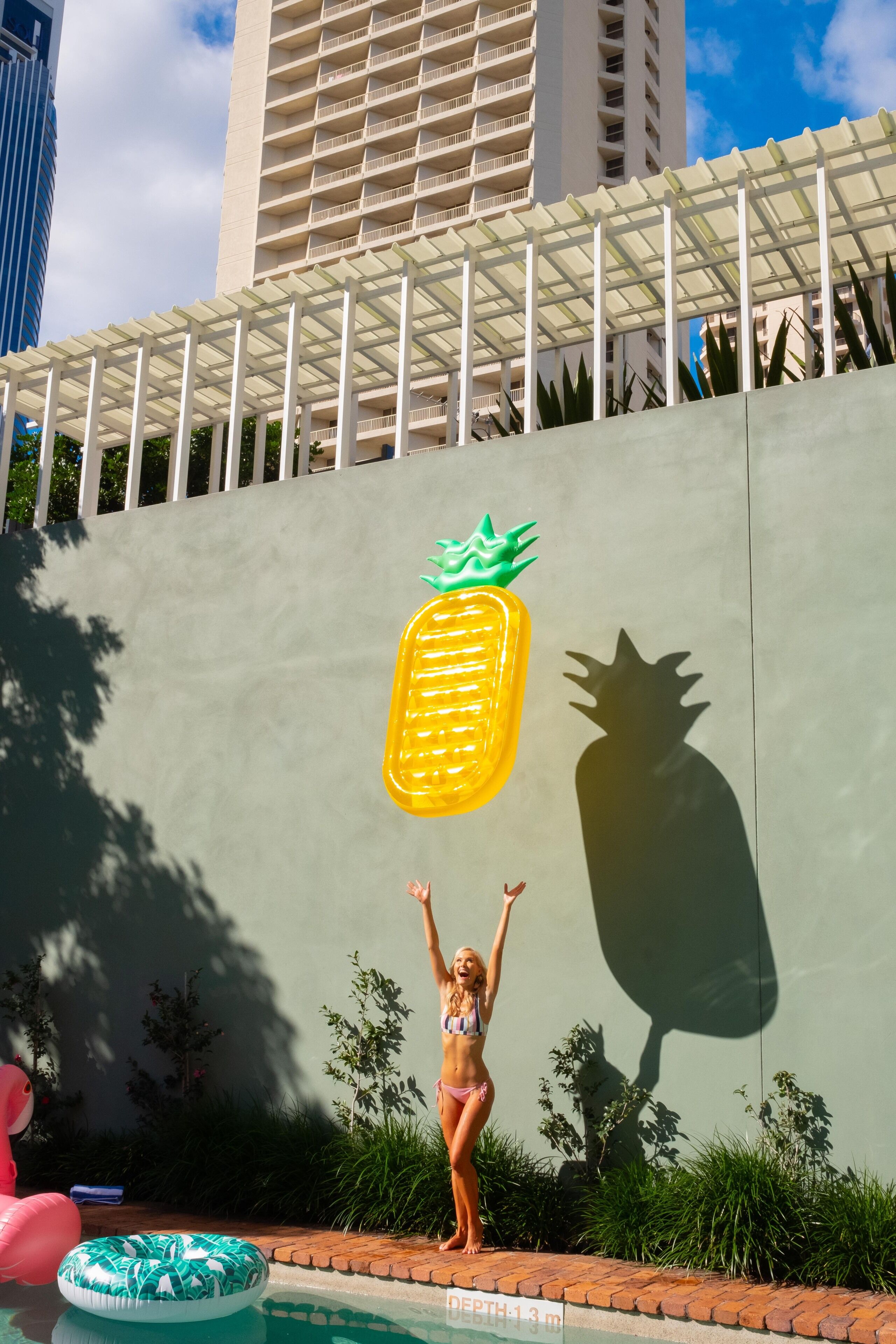 Una mujer en traje de baño de pie junto a una piscina con un gran mural de piña en la pared.