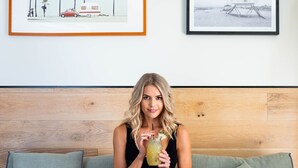 A person sitting on a sofa with a bowl of cereal and a drink, with two framed pictures on the wall behind. - The Island Gold Coast (Surfers Paradise)