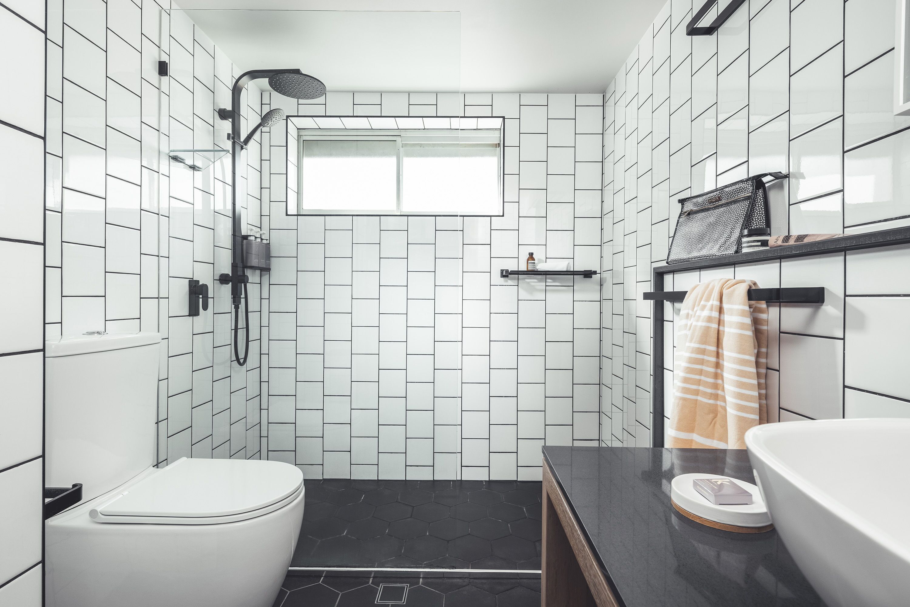 Une salle de bain moderne avec des carreaux noirs et blancs, des toilettes, un lavabo et un espace douche.