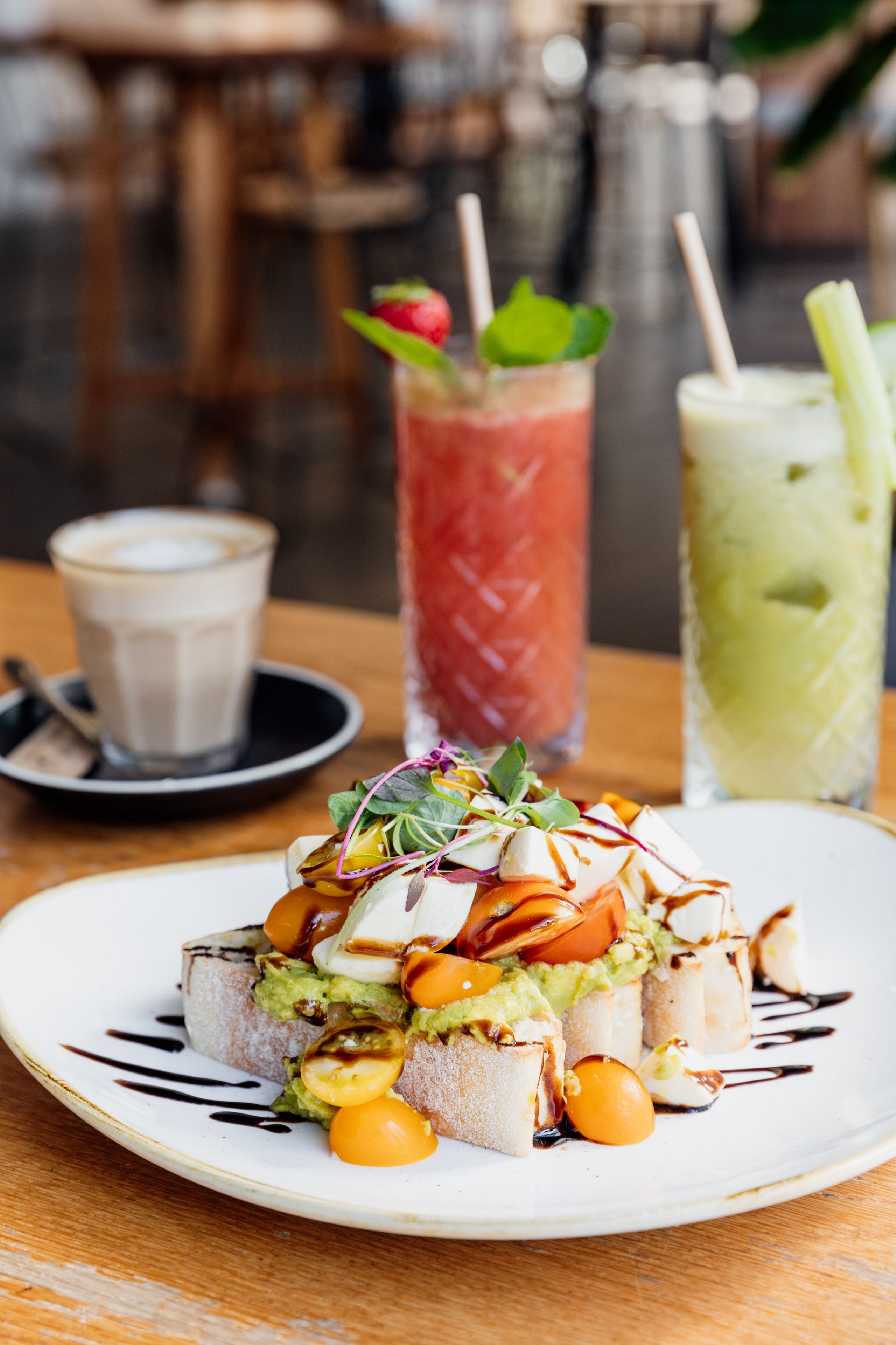 A plate with avocado toast topped with various ingredients and two drinks in the background.
