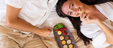A couple lying in bed with a remote control and a tray of chocolates.