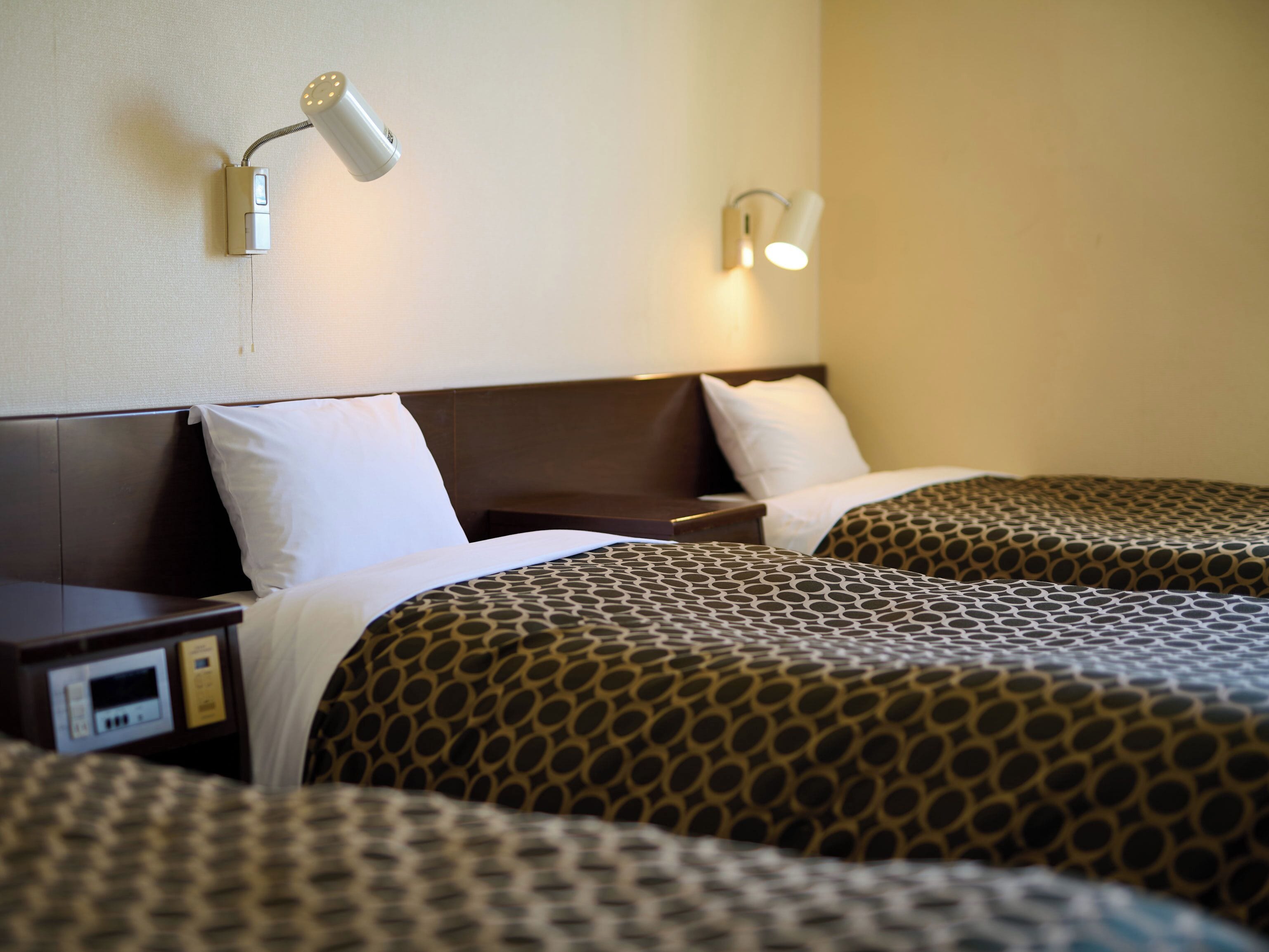 A hotel room with two beds, each with patterned bedding, a nightstand, and a wall-mounted lamp.