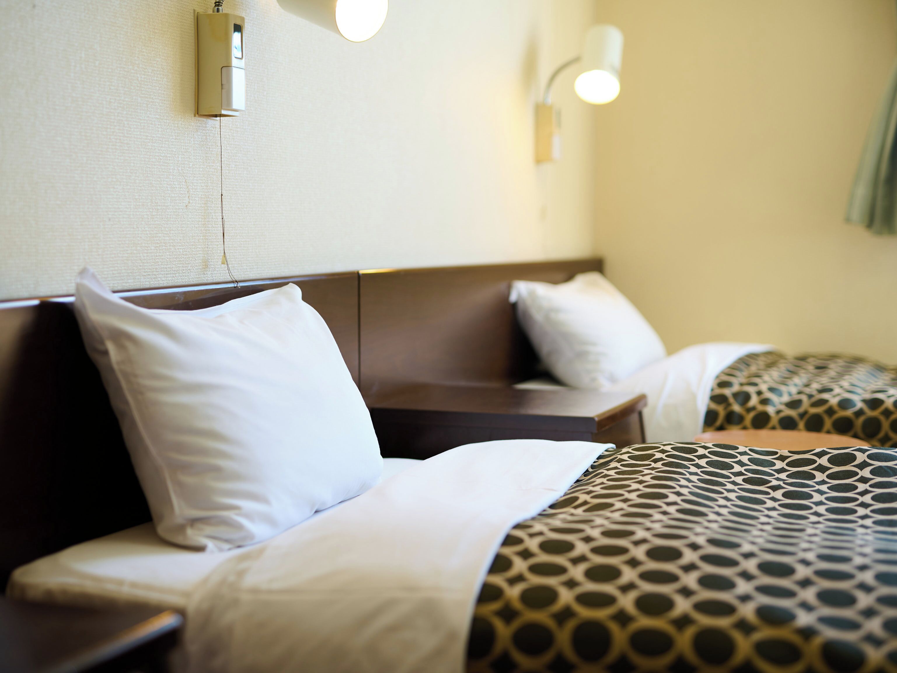 Habitación de hotel con dos camas, cada una con almohada y manta. Hay dos luces fijadas a la pared.