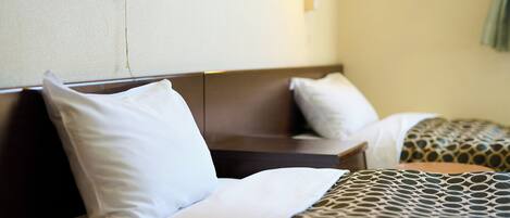 Habitación de hotel con dos camas, cada una con almohada y manta. Hay dos luces fijadas a la pared.