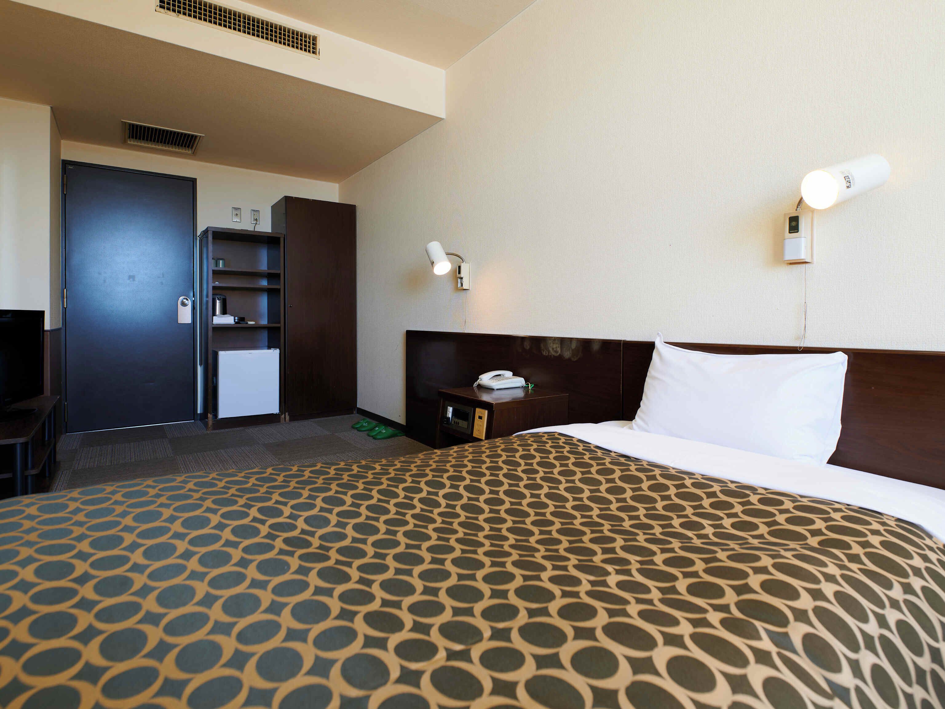 A hotel room with a bed, a desk, a wardrobe, and a minibar.