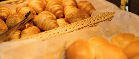 A display of assorted baked goods, including croissants and other pastries, arranged on a tray with a woven basket and a pair of tongs.