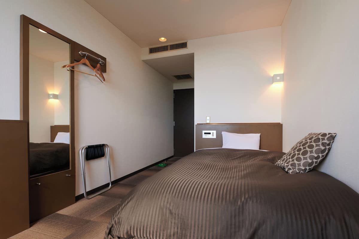 A hotel room with a large bed, a mirror, a bedside table, and a wall-mounted light.