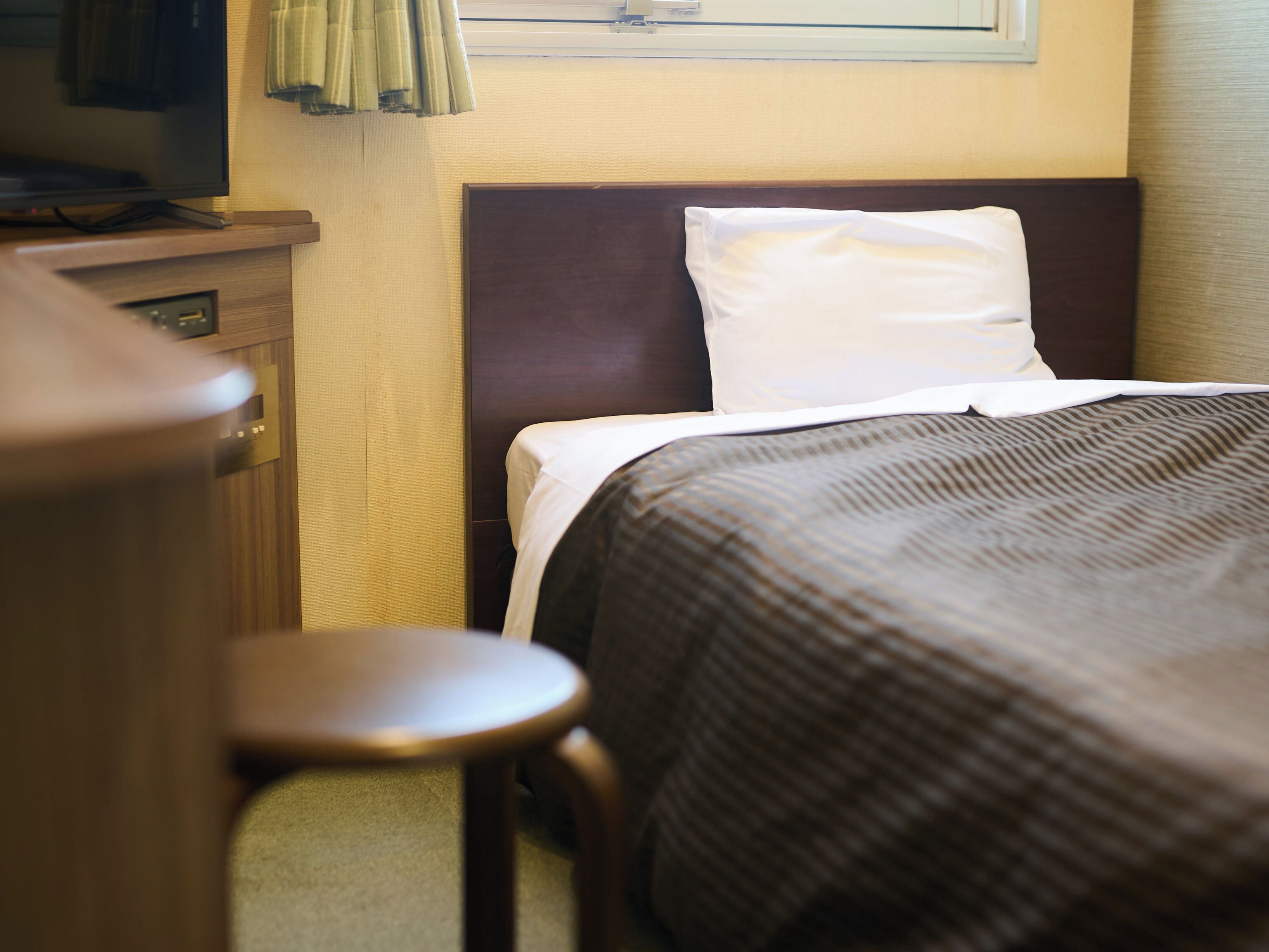 Una habitación de hotel con una cama, una mesita de noche de madera, un televisor y una ventana con cortinas.
