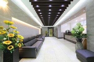 A reception area with a modern design, featuring a sofa, a large vase with flowers, and a reception desk.